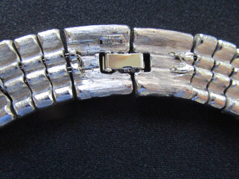 Puede incluir: Collar de metal plateado con un cierre que dice "BERNARD 1".