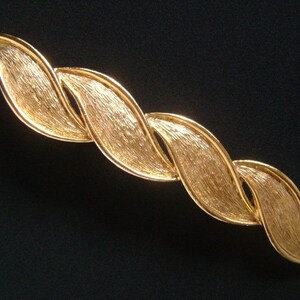 May include: A gold-toned, twisted, leaf-shaped brooch. The brooch is made of metal and has a brushed finish.