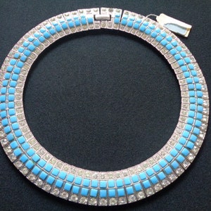 Puede incluir: Un collar de declaraci&oacute;n plateado y azul con un dise&ntilde;o geom&eacute;trico. El collar est&aacute; hecho de peque&ntilde;as piedras cuadradas engastadas en plata.