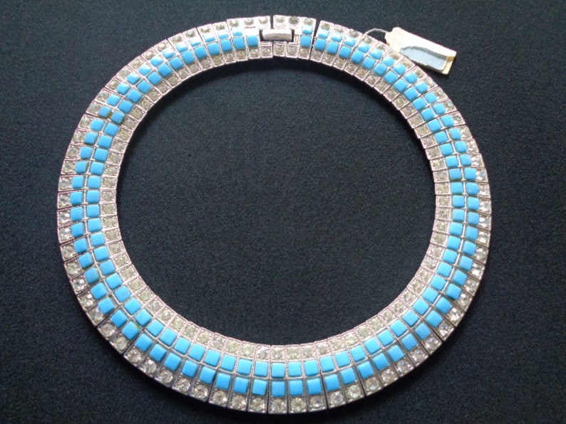 Puede incluir: Un collar de declaraci&oacute;n plateado y azul con un dise&ntilde;o geom&eacute;trico. El collar est&aacute; hecho de peque&ntilde;as piedras cuadradas engastadas en plata.