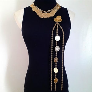 May include: A gold chain necklace with multiple strands and coin-shaped charms. The necklace is layered and has a long, dangling strand with additional coin charms.
