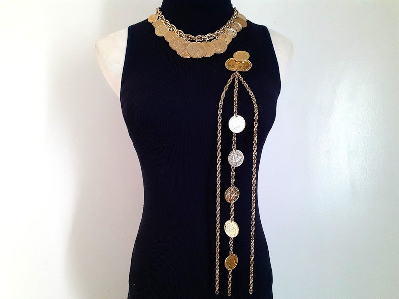 May include: A gold chain necklace with multiple strands and coin-shaped charms. The necklace is layered and has a long, dangling strand with additional coin charms.