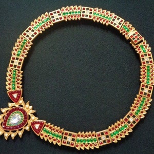 May include: A gold necklace with red, green, and white gemstones. The necklace has a pendant with a large white gemstone in the center.