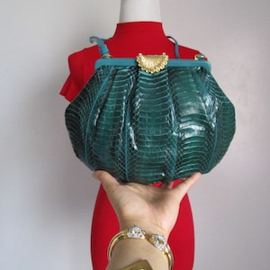 May include: A teal green snakeskin clutch bag with a gold clasp and a decorative gold accent on the front.