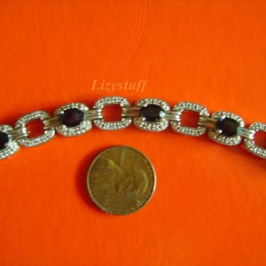 May include: A silver bracelet with square links and dark blue oval gemstones. The bracelet is shown next to a US penny for size comparison.