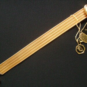 May include: A gold chain bracelet with a red and clear crystal charm. The bracelet has a decorative clasp with a gold design. The bracelet is labeled "Dorothy Booth".