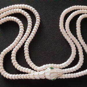 Peut inclure: Un collier de serpent en argent avec une t&ecirc;te sertie de pierres pr&eacute;cieuses vertes. Le collier est compos&eacute; de trois rangs de cha&icirc;ne en argent avec un motif &eacute;cailleux.