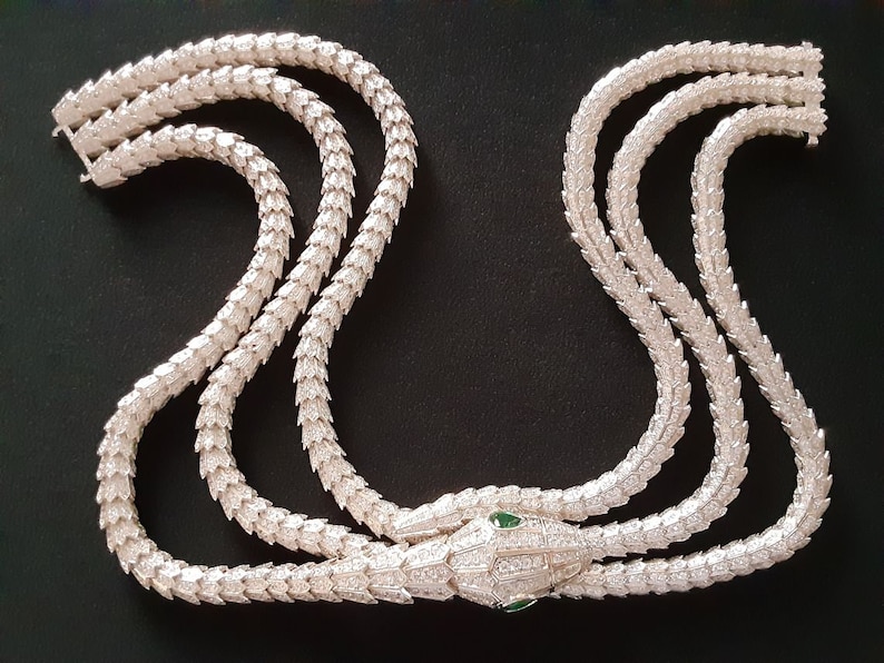 Peut inclure: Un collier de serpent en argent avec une t&ecirc;te sertie de pierres pr&eacute;cieuses vertes. Le collier est compos&eacute; de trois rangs de cha&icirc;ne en argent avec un motif &eacute;cailleux.