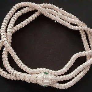 Peut inclure: Un collier de serpent en argent avec un design textur&eacute; d&eacute;taill&eacute;. La t&ecirc;te du serpent est orn&eacute;e de pierres pr&eacute;cieuses claires et vertes.