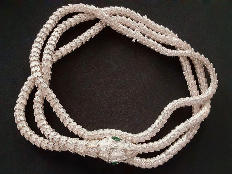 Peut inclure: Un collier de serpent en argent avec un design textur&eacute; d&eacute;taill&eacute;. La t&ecirc;te du serpent est orn&eacute;e de pierres pr&eacute;cieuses claires et vertes.