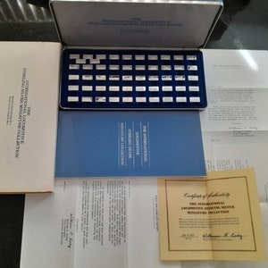May include: A collection of miniature sterling silver locomotives in a blue velvet box. The box is open and the locomotives are visible. The box is labeled "The International Locomotive Sterling Silver Miniature Collection".