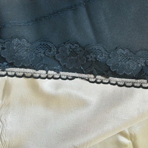 May include: A close-up of a beige fabric with a black lace trim. The lace is delicate and intricate, with a floral pattern.