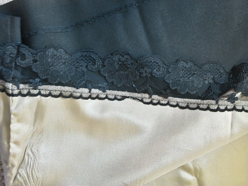 May include: A close-up of a beige fabric with a black lace trim. The lace is delicate and intricate, with a floral pattern.
