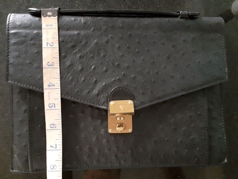 May include: A black ostrich leather briefcase with a gold lock and clasp. The briefcase has a flap closure and a handle.