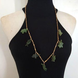May include: A gold chain necklace with green jade turtle and fish charms. The necklace is on a black background.