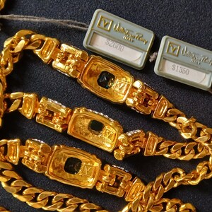 May include: Gold-toned chain necklaces with rectangular centerpieces and black accents. The necklaces have a thick curb chain design. Two tags are attached to the necklaces.