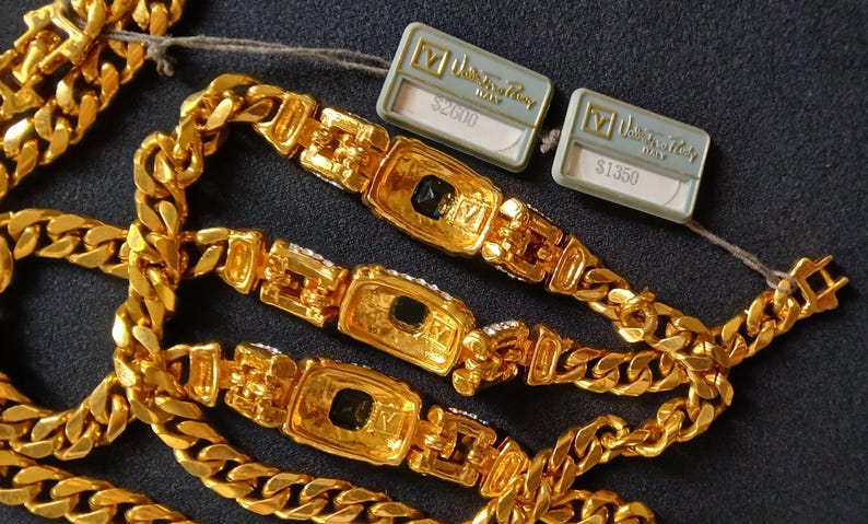 May include: Gold-toned chain necklaces with rectangular centerpieces and black accents. The necklaces have a thick curb chain design. Two tags are attached to the necklaces.
