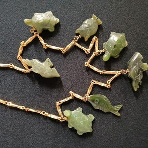 May include: A gold chain necklace with green jade pendants shaped like fish, turtles, and other sea creatures.