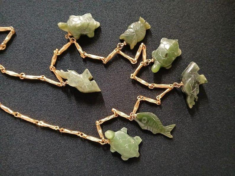 May include: A gold chain necklace with green jade pendants shaped like fish, turtles, and other sea creatures.