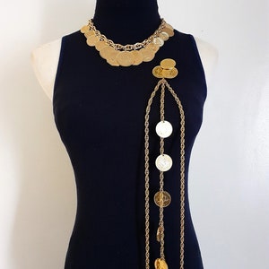 May include: A gold tone necklace with a long chain and multiple round coin-shaped charms. The necklace is layered with a shorter chain and more coin charms.