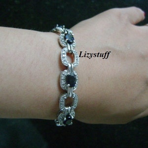 May include: A silver bracelet with a chain link design and oval-shaped blue gemstones set in a silver frame. The bracelet is adorned with small clear stones.