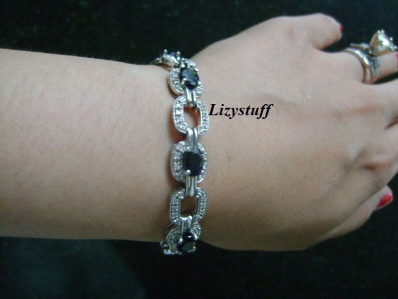 May include: A silver bracelet with a chain link design and oval-shaped blue gemstones set in a silver frame. The bracelet is adorned with small clear stones.