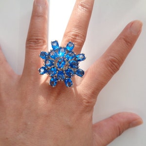 May include: A silver ring with a large blue gemstone cluster in the shape of a flower.