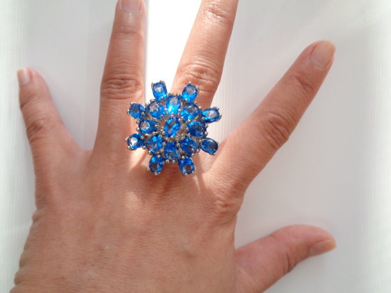 May include: A silver ring with a large blue gemstone cluster in the shape of a flower.