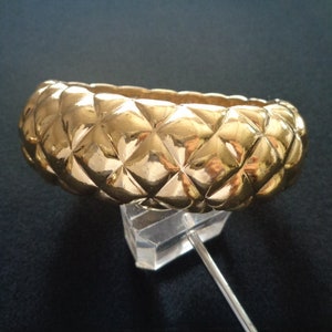 May include: A gold-toned bangle bracelet with a textured, quilted design.