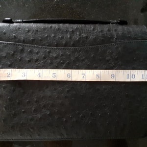 May include: Black ostrich leather clutch with a top handle and a zipper closure. The clutch measures 13 inches in length.