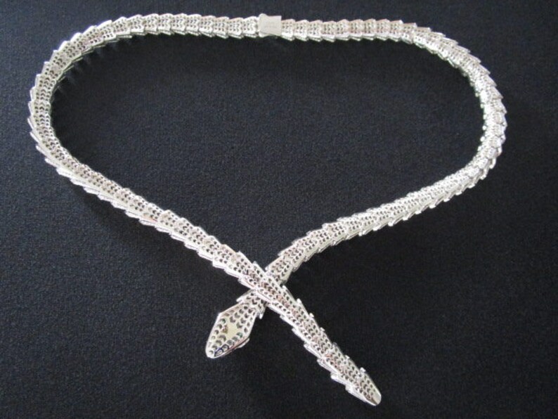 Op de afbeelding: Een zilveren slangenketting met een gedetailleerd, gestructureerd ontwerp. De ketting is gemaakt van kleine, in elkaar grijpende schakels die een slangvorm vormen. De ketting is een statementstuk dat elke outfit een vleugje elegantie zou geven.