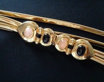 May include: A gold-tone chain belt with three rows of linked metal. The belt has three decorative heart-shaped clasps with pink and black oval stones.