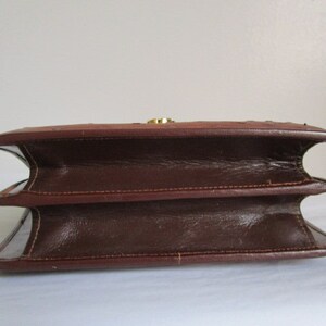 May include: A brown leather handbag with a flap closure and a gold-toned clasp. The bag has a structured shape and a double-layered design.