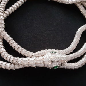 Peut inclure: Un collier de serpent en argent avec un pendentif t&ecirc;te de serpent. Le serpent est recouvert de petites pierres claires et la t&ecirc;te a deux pierres vertes pour les yeux.