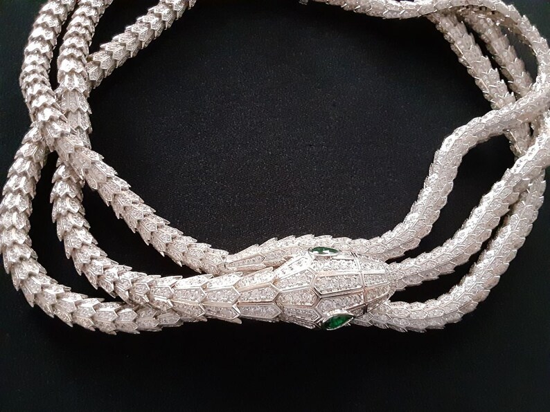 Peut inclure: Un collier de serpent en argent avec un pendentif t&ecirc;te de serpent. Le serpent est recouvert de petites pierres claires et la t&ecirc;te a deux pierres vertes pour les yeux.