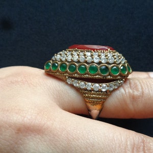 May include: A gold ring with a red stone and green stones set in a silver band.