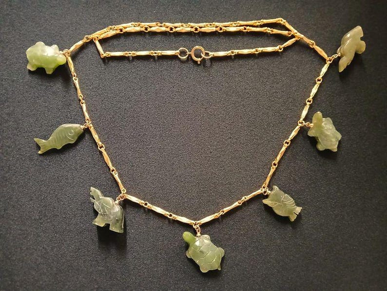 May include: A gold chain necklace with green jade pendants shaped like fish, turtles, and elephants.