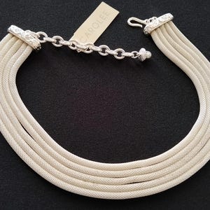 May include: A multi-strand silver-tone necklace featuring five parallel mesh chains connected by ornate, engraved metal end caps. The necklace includes an adjustable chain with a hook clasp and a small tag labelled CAROLEE attached to the hardware.