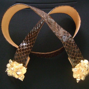 May include: A brown snakeskin belt with gold-toned decorative buckles. The belt is made of genuine leather and has a classic design.