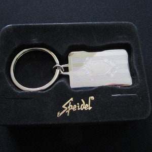 May include: A silver key chain with a blank rectangular tag. The tag has an engraved design and the word "Speidel" is printed on the black velvet box.