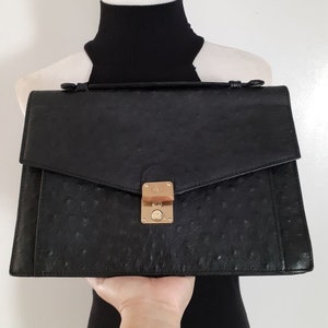 May include: Black ostrich leather briefcase with a gold clasp and a single handle.