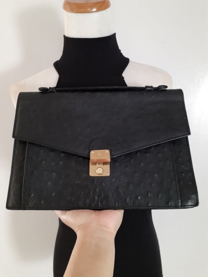 May include: Black ostrich leather briefcase with a gold clasp and a single handle.