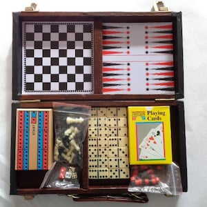 May include: A brown wooden travel game case with a variety of games inside, including a chessboard, checkers, dominoes, and playing cards. The case has a latch and a handle.