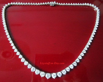 May include: A silver necklace with a row of clear round stones. The necklace is on a red background.