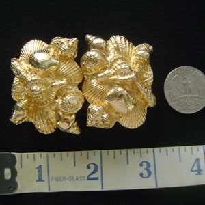 May include: A pair of gold-tone metal belt buckles with a seashell design. The buckles are about 2 inches long.