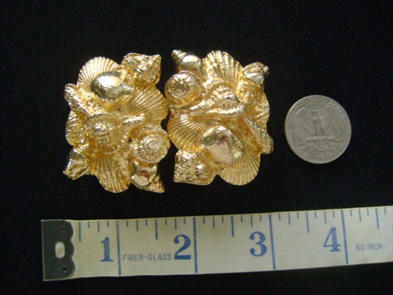 May include: A pair of gold-tone metal belt buckles with a seashell design. The buckles are about 2 inches long.