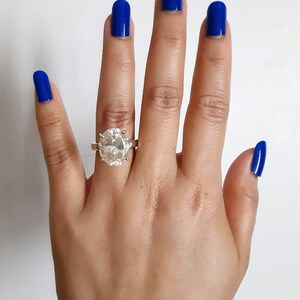 Op de afbeelding: Een hand met blauwe nagellak draagt een grote, heldere, ovale diamanten ring aan de ringvinger.