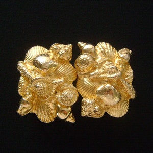 May include: A pair of gold-tone metal shell-shaped brooches. Each brooch is detailed with multiple raised shell shapes.