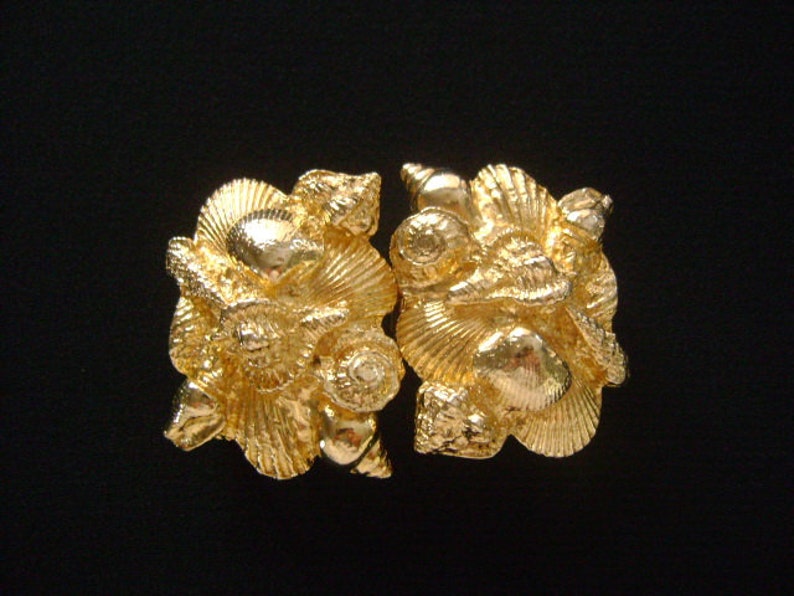 May include: A pair of gold-tone metal shell-shaped brooches. Each brooch is detailed with multiple raised shell shapes.