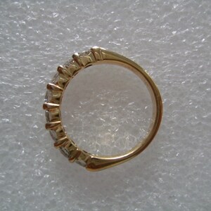 May include: A gold band ring with a row of clear gemstones set in the band.